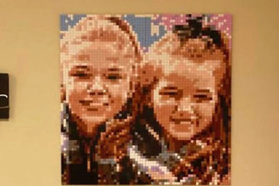 A finished brick mosaic of two smiling sisters hanging on a family room wall